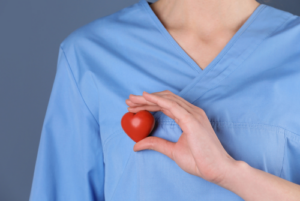 Person in scrubs holding a red stressball heart over their heart